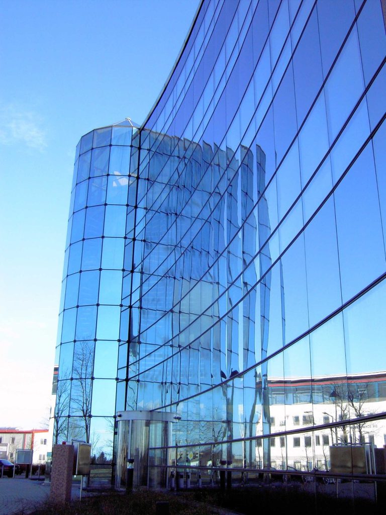 Glasfassade eines modernen Gebäudes mit gewellten Linien und reflektierendem Himmel.